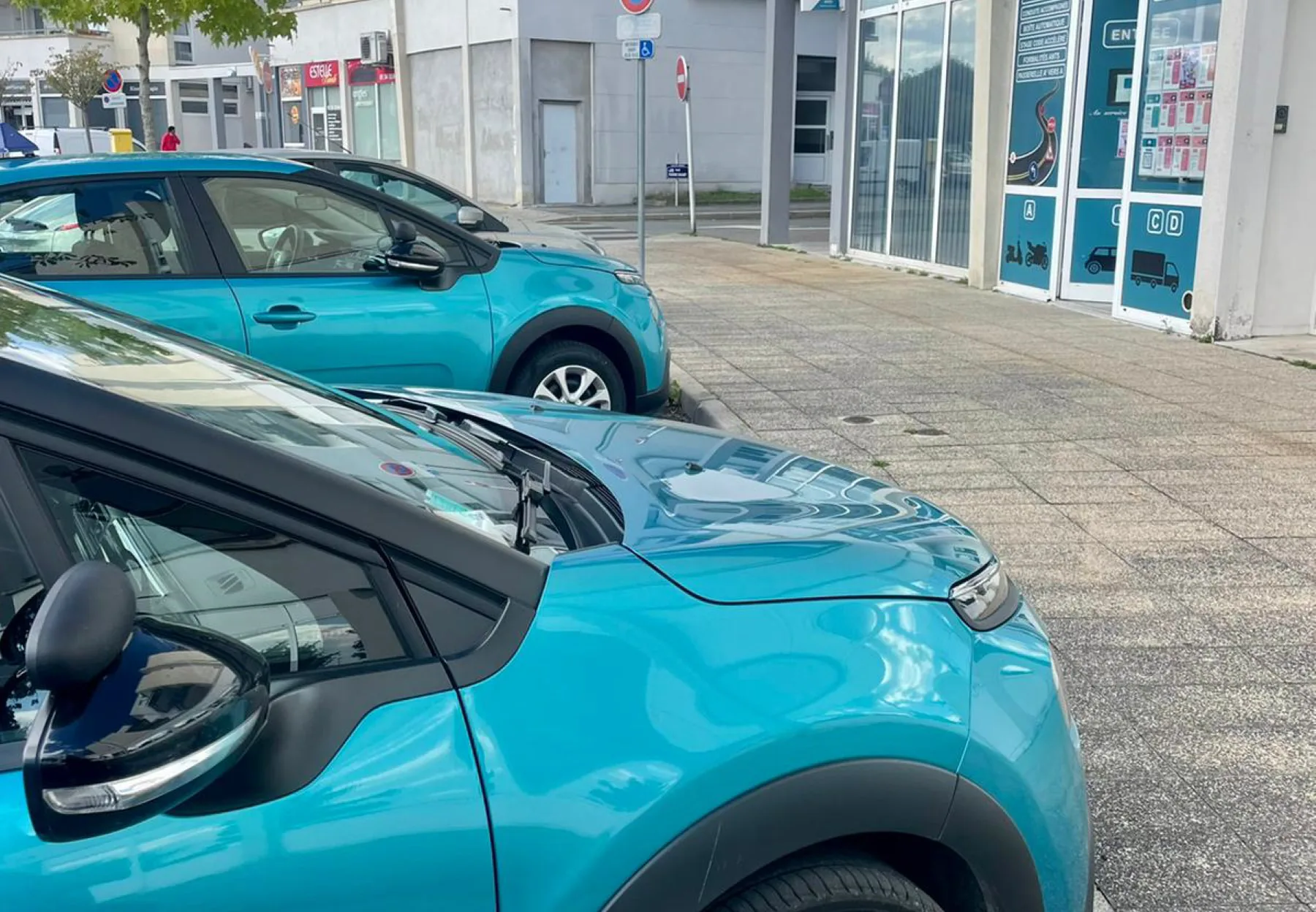 Les Citroën C3 turquoise de JD Auto Moto École garées devant la vitrine de l'agence