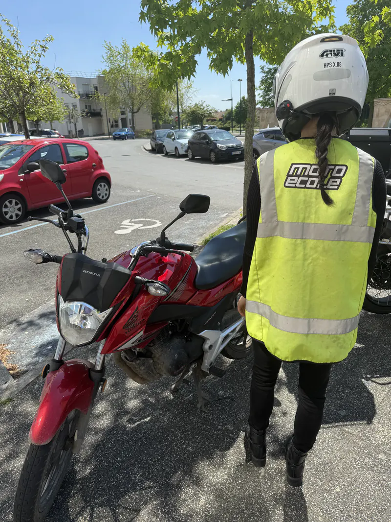 Élève en gilet « moto école » devant une Honda rouge